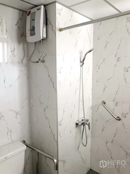 Apartment for rent in Suan Luang, Bangkok - Modern bathroom with marble-effect tiles, walk-in shower, handheld shower, water heater and safety grab bars.