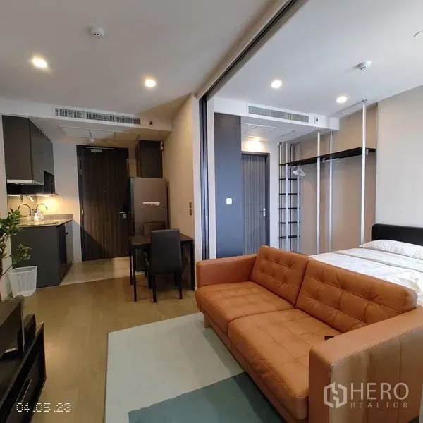 Condominium for rent in Watthana, Bangkok - Open-plan living area with kitchenette, orange sofa and sliding partition to the bedroom.