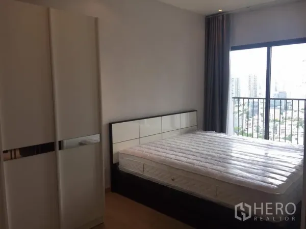Condominium for rent in Khlong Toei, Bangkok - Bedroom with large window and balcony railing, city skyline view, bed frame and wardrobe.