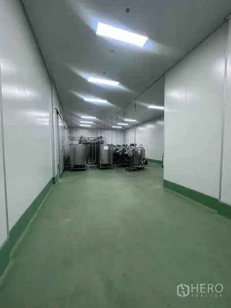 工厂 出租 - GMP级洁净室走廊，绿色环氧地坪，尽头有不锈钢储罐与明亮LED照明。