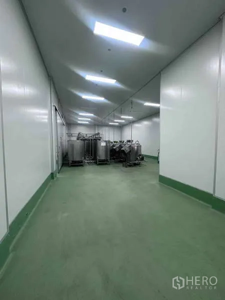 工厂 出租 - GMP级洁净室走廊，绿色环氧地坪，尽头有不锈钢储罐与明亮LED照明。