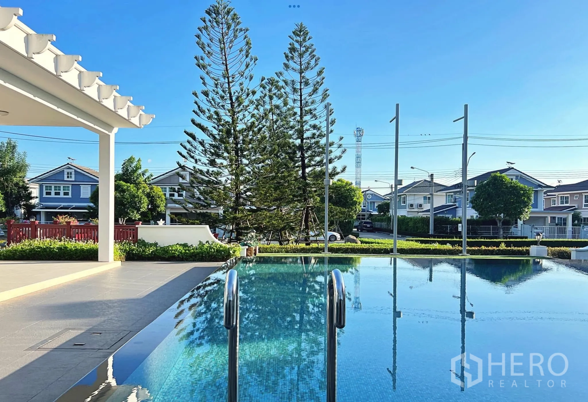 Townhouse for rent or sale in Sai Mai, Bangkok - Outdoor swimming pool beside the clubhouse with trees and blue sky.