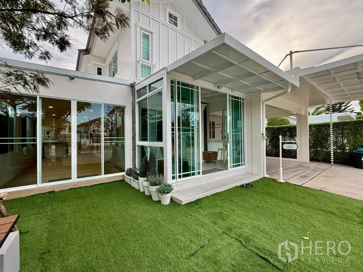 Detached House for rent in Bang Phli, Samut Prakan - Corner view of glass-walled sunroom opening to a neat synthetic lawn.