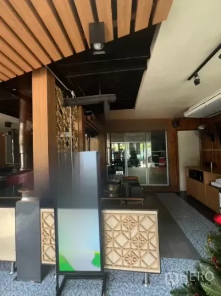 零售空间 出租在Watthana, Bangkok - 入口室内采用木质装饰与镂空屏风，配有座位并通向玻璃门。