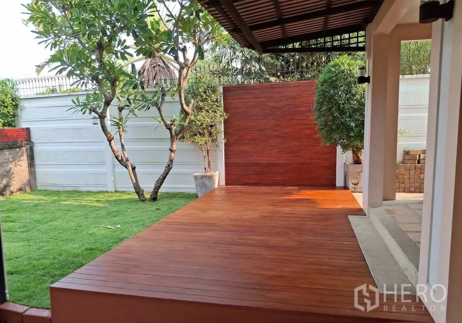 บ้าน ให้เช่า - ชานพักมีหลังคามองเห็นสนามหญ้าและกำแพงสูงพร้อมต้นไม้