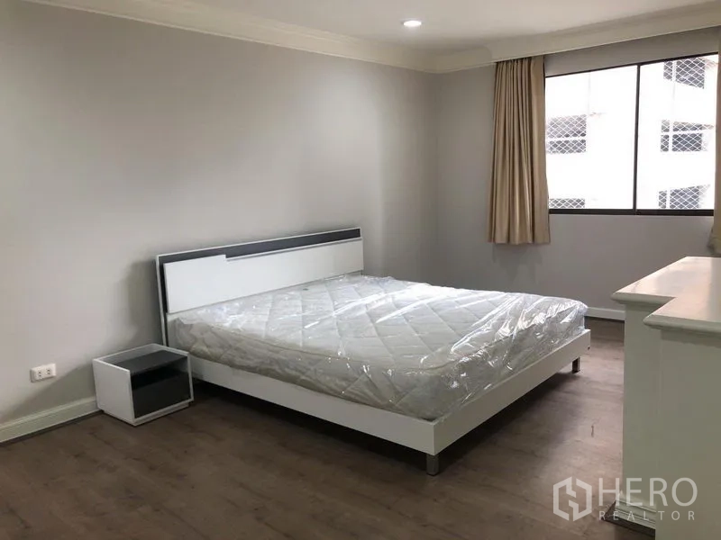 Condominium for rent in Watthana, Bangkok - Calm bedroom with large window, queen bed, bedside table, neutral walls and wood flooring.