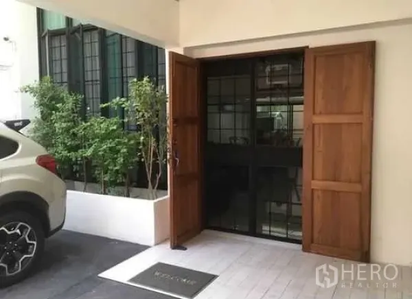 Townhouse for rent in Bang Rak, Bangkok - Covered parking area and townhouse entrance with wooden double doors and black metal gate.
