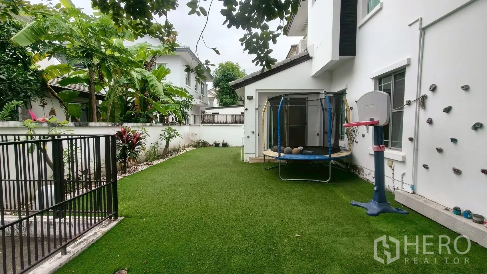 บ้าน ให้เช่าหรือขายในMueang Samut Prakan, Samut Prakan - สนามหญ้าเทียมกว้างข้างบ้าน มีแทรมโพลีน ห่วงบาส และจุดปีนผนัง ท่ามกลางต้นไม้