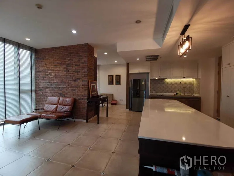 Condominium for rent or sale in Bang Rak, Bangkok - Living area and kitchen with extended island, brick accent wall, and lounge seating.