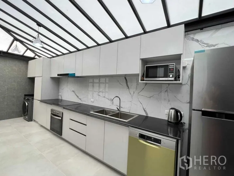 联排别墅 出租在Wang Thonglang, Bangkok - 现代厨具视角：双槽水槽、烤箱、微波炉、洗碗机与高柜。