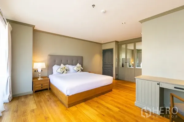 房间 出租在Khlong Toei, Bangkok - 宽敞卧室，软包床头，床头灯，镜面衣柜与工作桌。