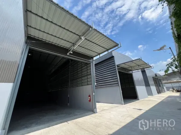 货栈 出租在Prawet, Bangkok - 现代灰色仓库排，超大卷闸门与带顶装卸区，宽阔混凝土通道。