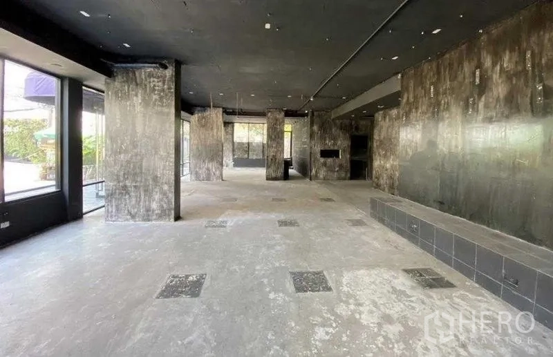 零售空间 出租在Khlong Toei, Bangkok - 开放式零售大厅，混凝土柱与黑色吊顶，临街玻璃面。