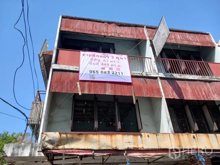 Shophouse for rent or sale in Bang Khen, Bangkok - Upper floors of a weathered corner shophouse with red metal awnings and balcony railings.