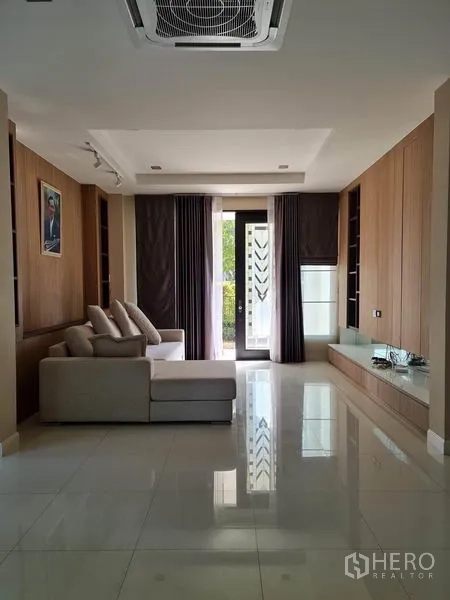 独立式住宅 出售在Khlong Toei, Bangkok - 明亮客厅，L形沙发，木质墙面，亮面瓷砖地，吊顶空调与带窗帘的玻璃门。