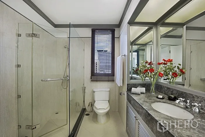 Condominium for rent in Khlong San, Bangkok - Bathroom with glass shower enclosure, stone-top vanity, mirrors and window.