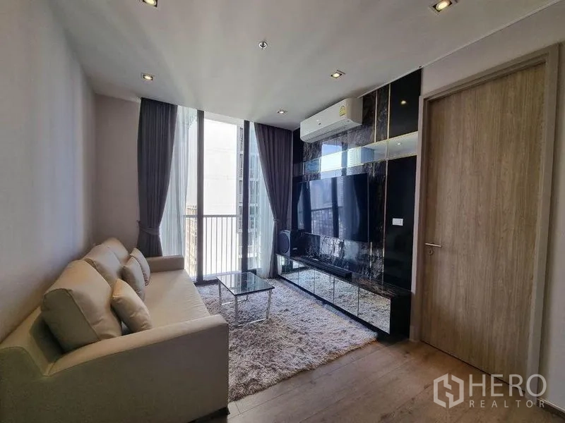 คอนโด ขาย - ห้องนั่งเล่นผนังทีวี พรมขนฟู และประตูกระจกสไลด์ออกระเบียง ในคอนโดสุขุมวิท