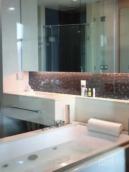Condominium for sale in Ratchathewi, Bangkok - Close-up of jetted bathtub with mosaic tile backsplash and glass partition in a modern bathroom.