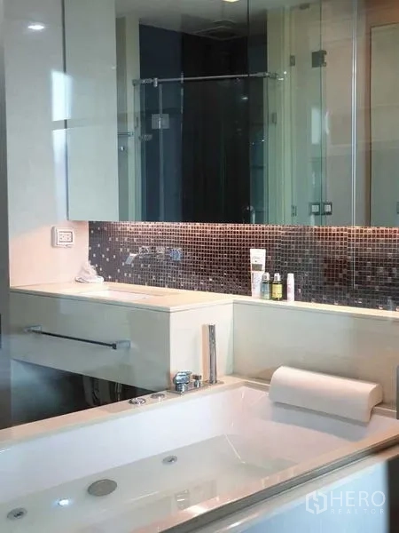 Condominium for sale in Ratchathewi, Bangkok - Close-up of jetted bathtub with mosaic tile backsplash and glass partition in a modern bathroom.