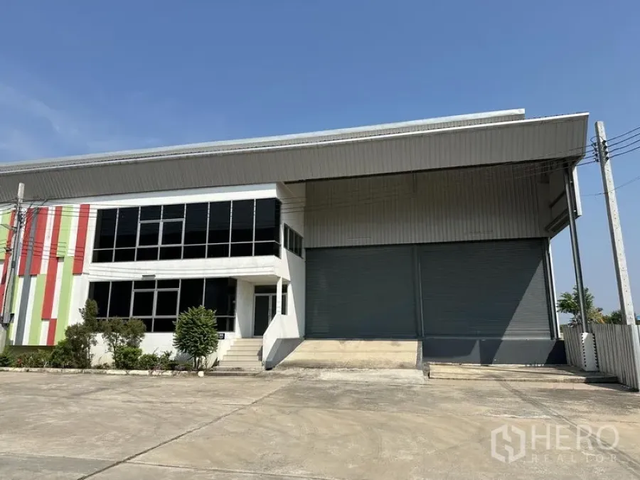 Warehouse for rent in Samut Prakan - Modern warehouse exterior with large roller shutter, covered loading dock, and glazed office block.