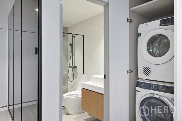 Condominium for rent in Watthana, Bangkok - Contemporary bathroom with glass shower next to a closet housing stacked washer and dryer.