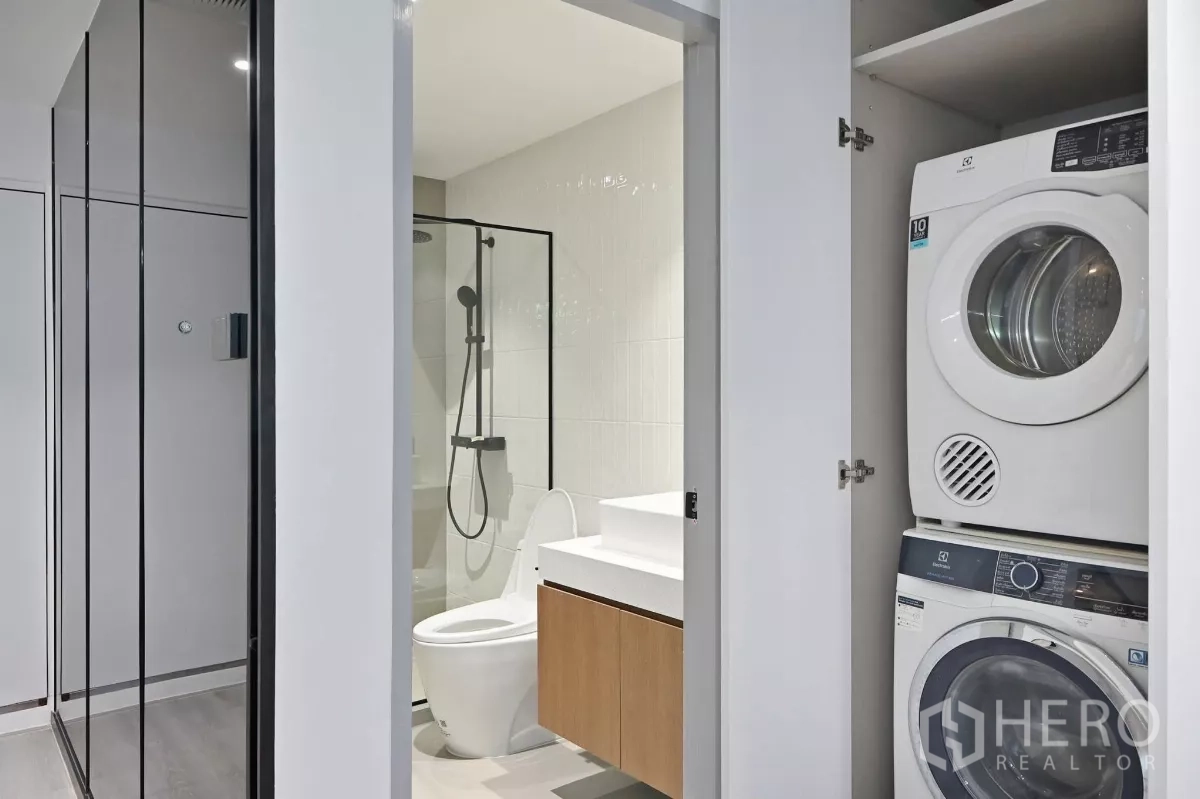 Condominium for rent in Watthana, Bangkok - Contemporary bathroom with glass shower next to a closet housing stacked washer and dryer.