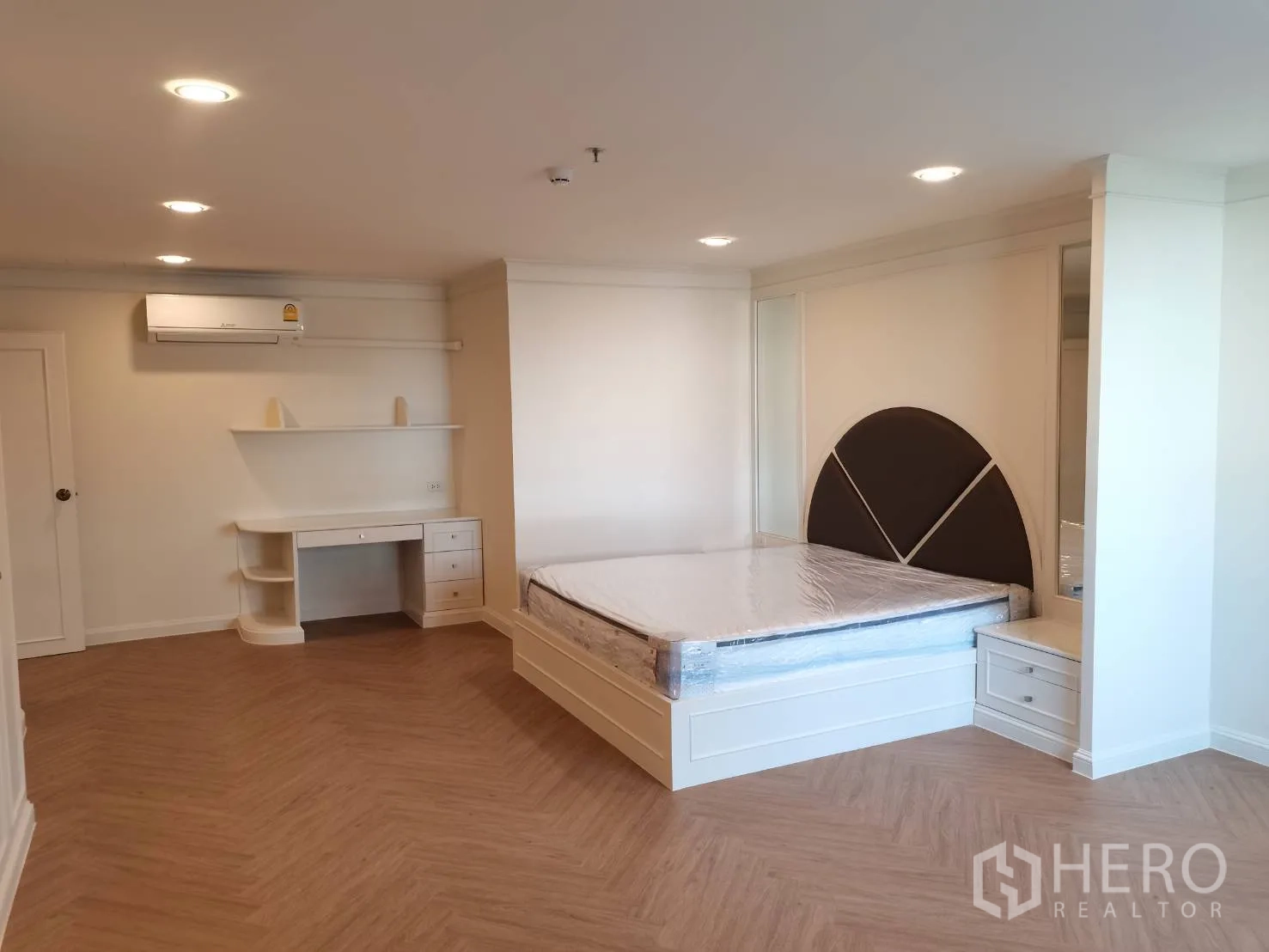 Condominium for rent in Watthana, Bangkok - Spacious bedroom with wood floors, built-in desk, and padded headboard.