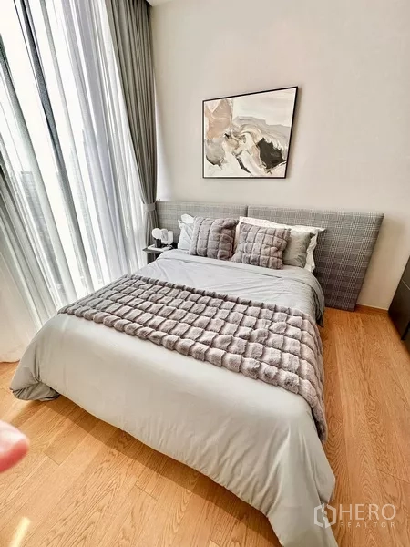 Condominium for rent in Pathum Wan, Bangkok - Guest bedroom with a gray upholstered headboard, plush throw, and sheer curtains.