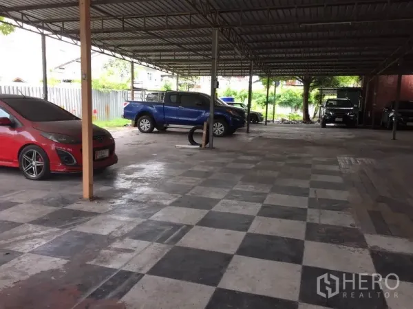 Warehouse for rent in Pathum Thani - Wide checkerboard-floor loading zone under a metal canopy with parked vehicles.