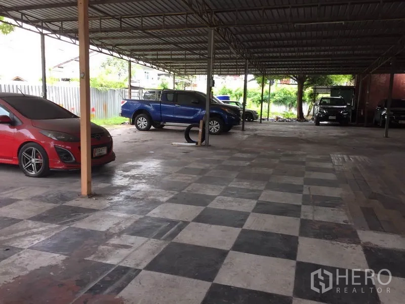 Warehouse for rent in Pathum Thani - Wide checkerboard-floor loading zone under a metal canopy with parked vehicles.