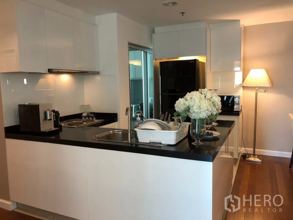 Condominium for rent in Huai Khwang, Bangkok - Compact U‑shaped kitchen with black countertops, built‑in hob, hood and floor lamp.