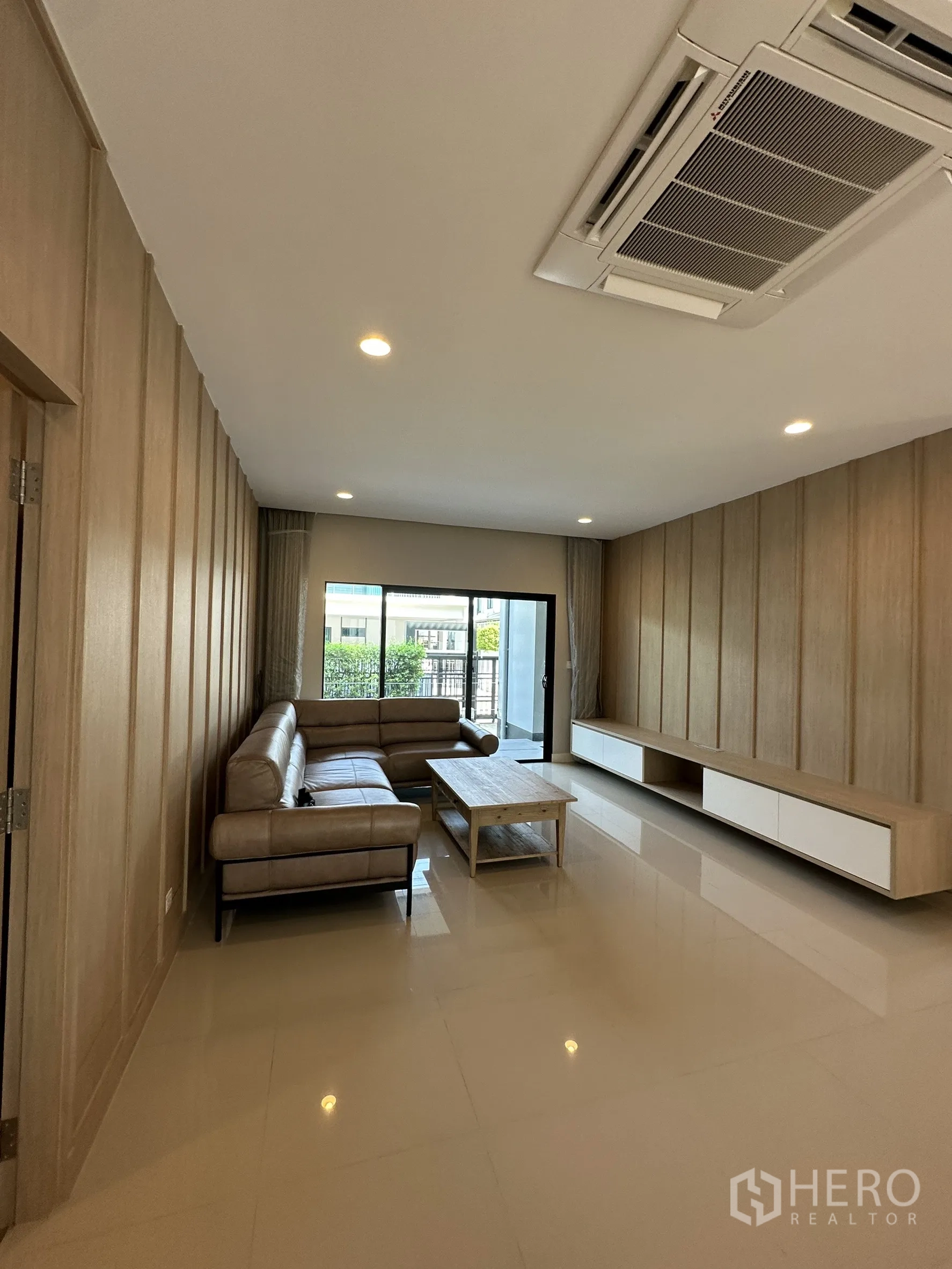 บ้าน ขายในLam Luk Ka, Pathum Thani - ห้องนั่งเล่นสว่าง โซฟาหนังรูปตัวแอล ผนังลายไม้ และแอร์ฝังฝ้า