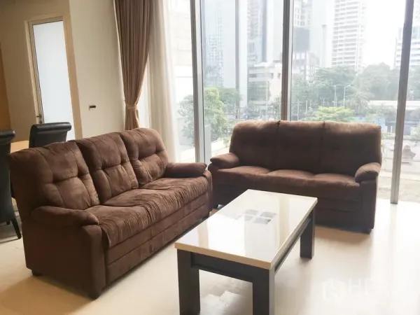 Condominium for rent in Bang Rak, Bangkok - Bright living room with two brown sofas and a coffee table by floor-to-ceiling windows with a city view.