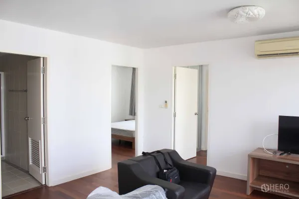 คอนโด ให้เช่าในWatthana, Bangkok - ห้องนั่งเล่นผนังสีขาว พื้นไม้ และประตูเชื่อมไปยังห้องนอนกับห้องน้ำ