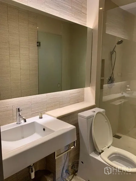 Condominium for rent - Guest bathroom with glass shower, toilet and wide vanity mirror.
