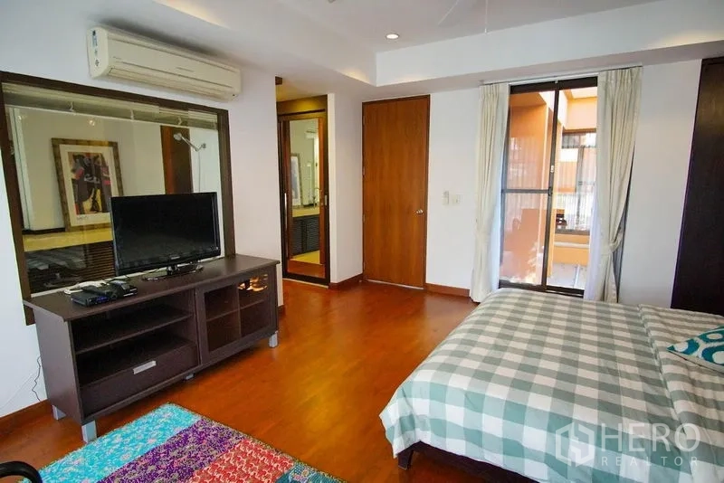 Townhouse for rent in Watthana, Bangkok - Master bedroom view with TV console, balcony door, and hardwood floors.