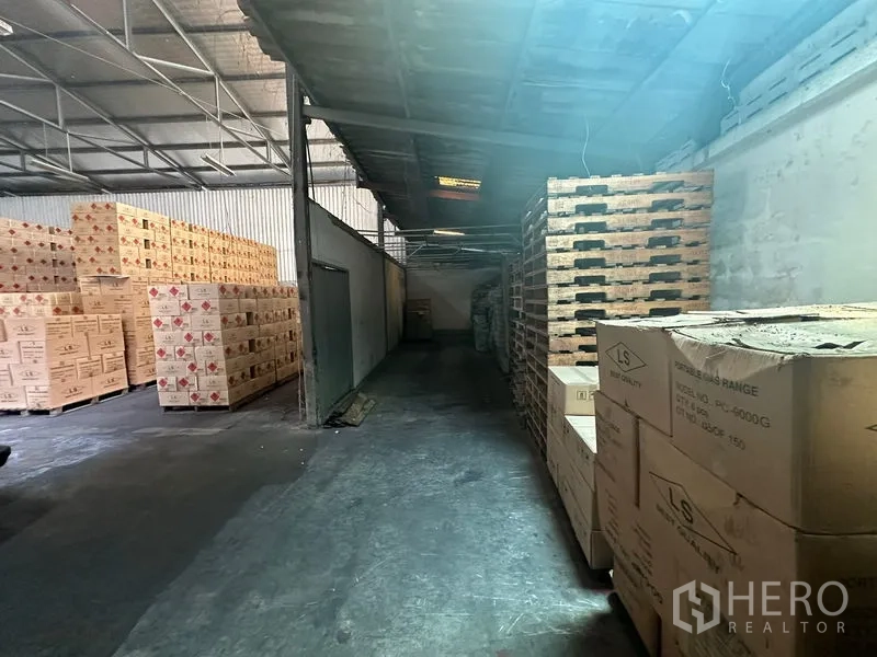 Warehouse for rent in Suan Luang, Bangkok - Narrow side aisle with pallets and boxes along a corrugated wall.