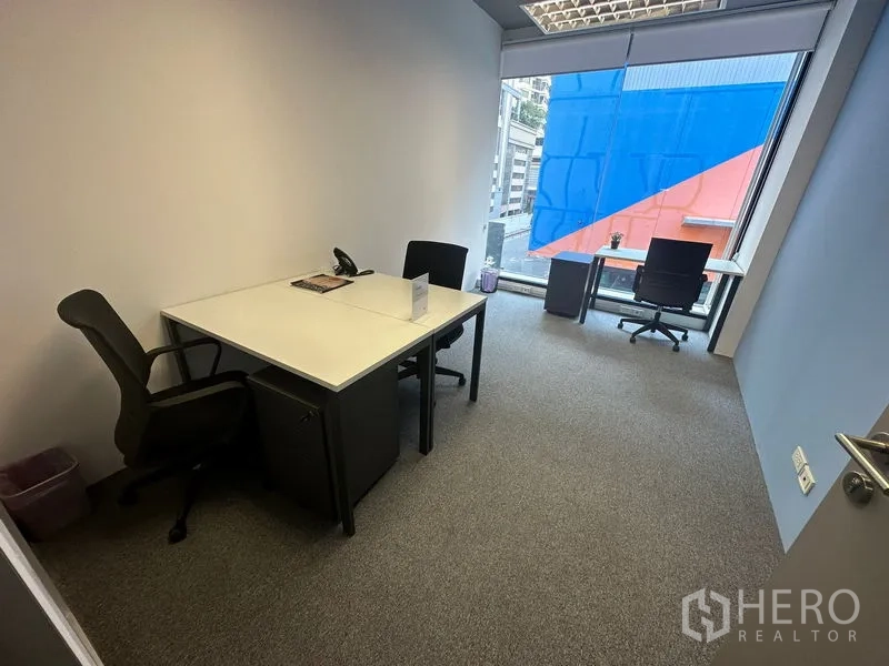 Office Space for rent in Khlong Toei, Bangkok - Furnished 12 sqm private office with two desks, ergonomic chairs, carpet flooring, and a large window with city outlook near BTS Phrom Phong.