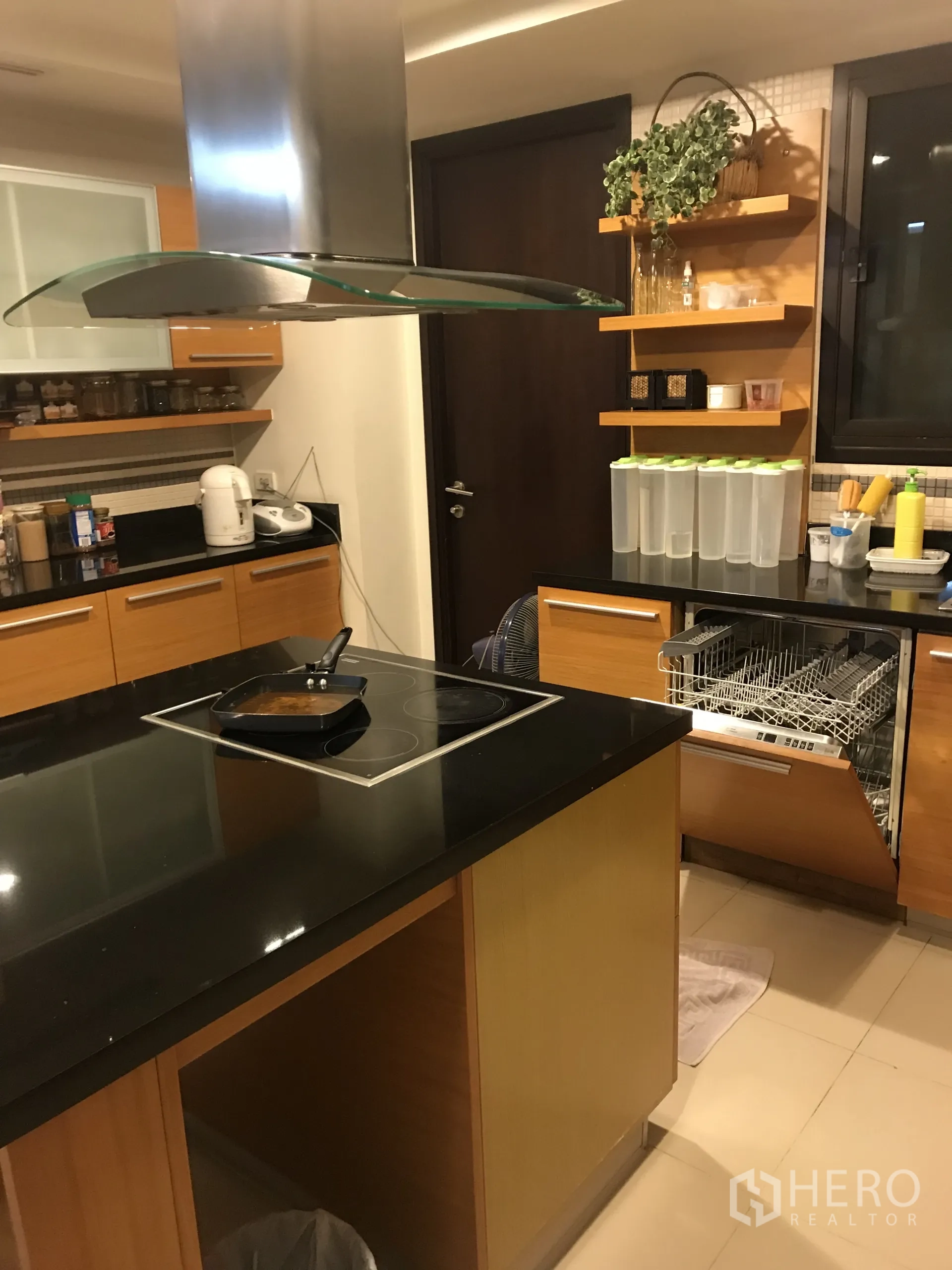 Condominium for sale in Yan Nawa, Bangkok - Modern kitchen with island cooktop, stainless hood, black stone counters and dishwasher.