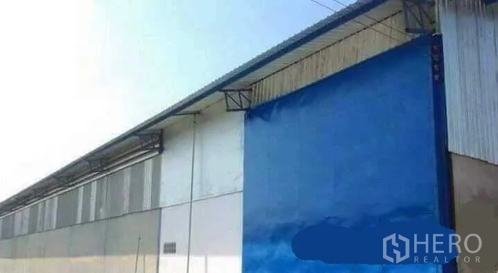 工厂 出租在Mueang Nakhon Pathom, Nakhon Pathom - 工厂侧立面，配大型蓝色金属推拉门与金属屋面。