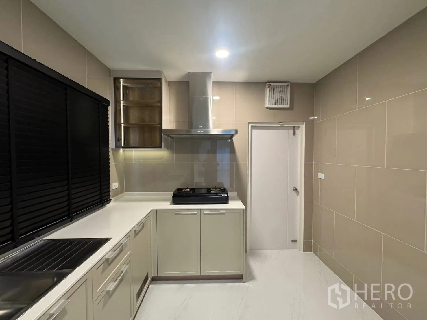 Detached House for rent in Bang Phli, Samut Prakan - L-shaped kitchen with white cabinets, gas hob, range hood, and black blinds.