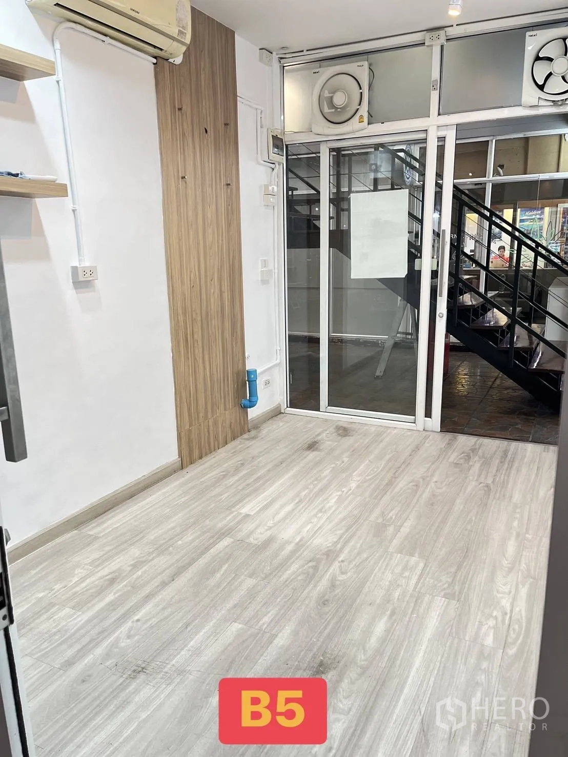 Retail Space for rent in Watthana, Bangkok - Interior of a small retail space showing wood-look floor, wall air-conditioner, wooden accent panel, and glass storefront with extractor fans.