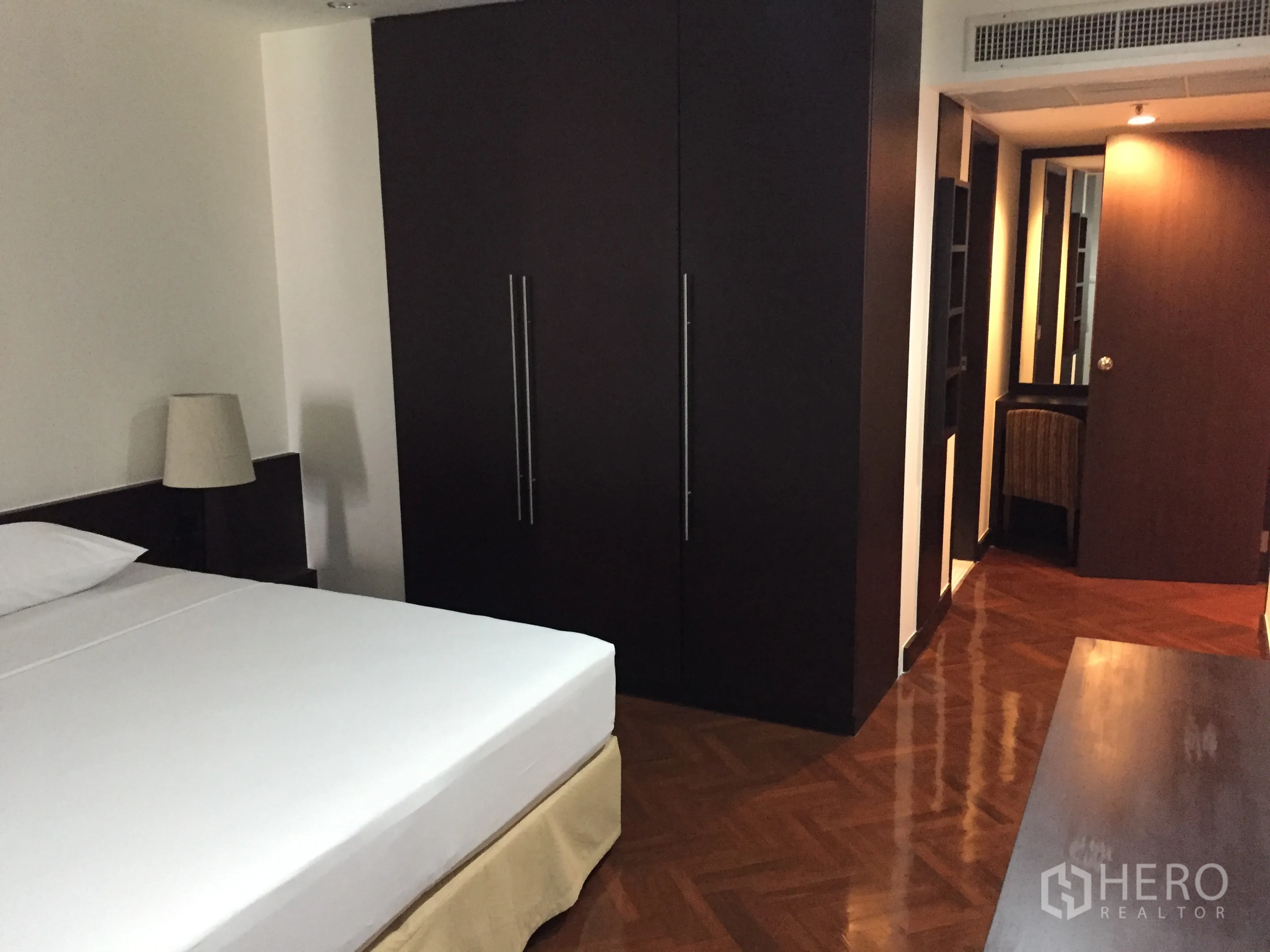 Condominium for rent in Watthana, Bangkok - Master bedroom with dark wood wardrobes and polished parquet floors.