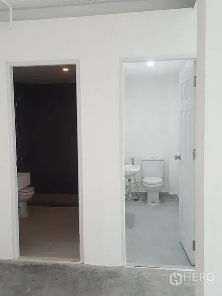 Home Office for rent in Khlong Toei, Bangkok - Two bathrooms side by side, one dark-tiled wet room and one bright white toilet.