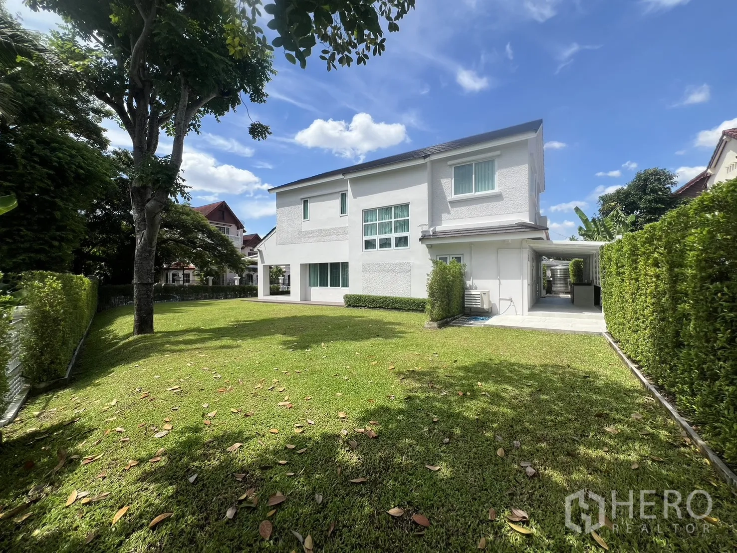 独立式住宅 出租在Mueang Samut Prakan, Samut Prakan - 后院大片草坪，成树掩映在白色房屋后。