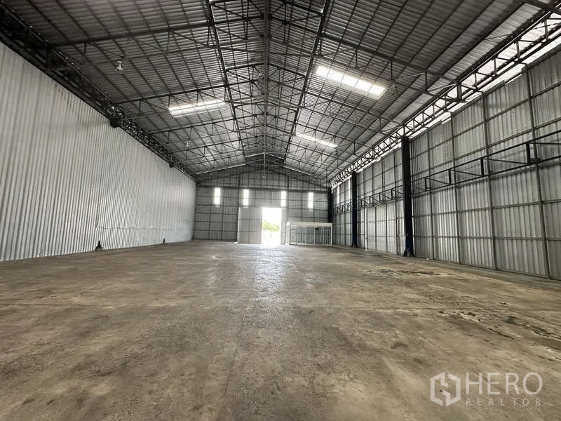 Warehouse for rent in Pak Kret, Nonthaburi - Deep warehouse interior toward the main entrance under a tall steel truss roof.