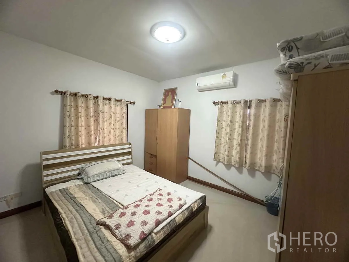 独立式住宅 出售在Pathum Thani - 带空调的卧室，双人床、衣柜和窗帘。