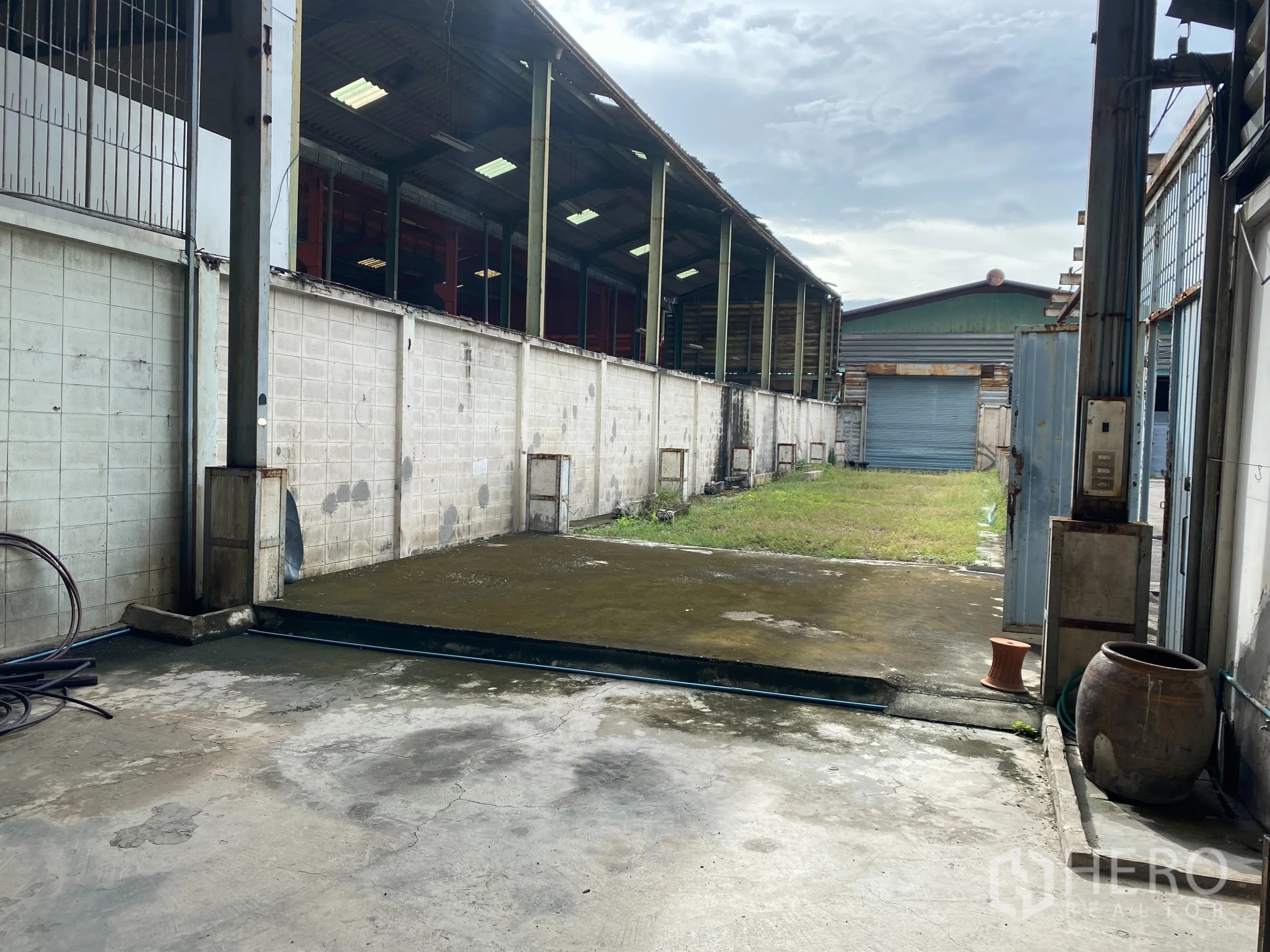 零售空间 出租在Yan Nawa, Bangkok - 露天院落与混凝土通道，通往蓝色卷闸门，部分区域有屋顶。