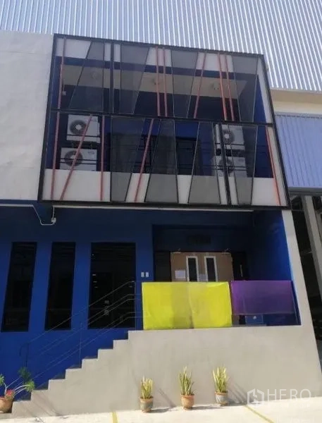 Warehouse for rent in Bang Phli, Samut Prakan - Modern warehouse facade with blue accent walls, a glass-front office and stairway entrance.