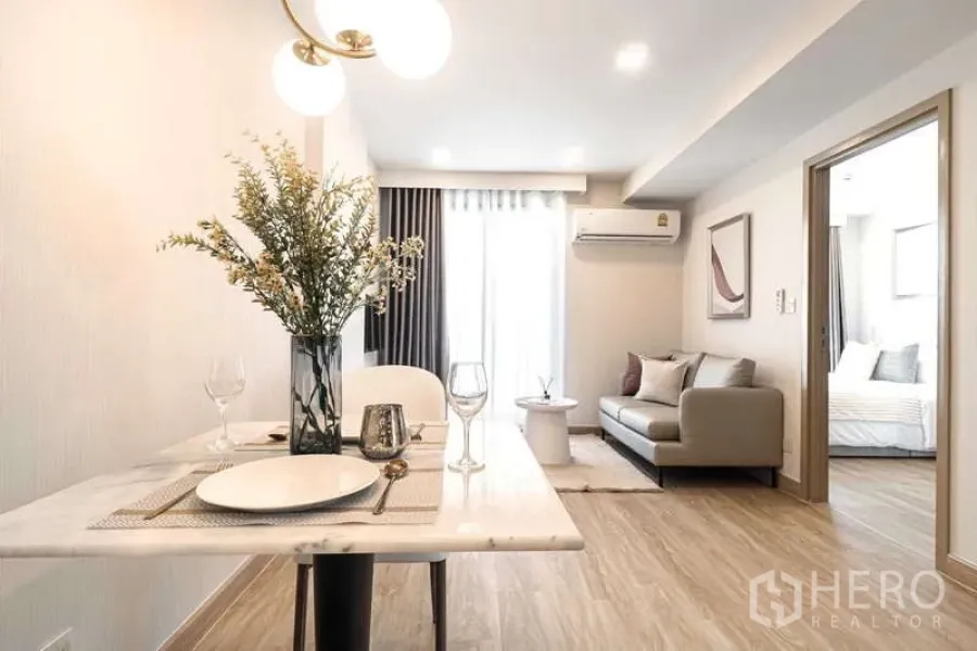 คอนโด ให้เช่า - มุมมองจากโซนทานอาหารสู่ห้องนั่งเล่น มีโคมไฟแขวนและโซฟาติดระเบียง